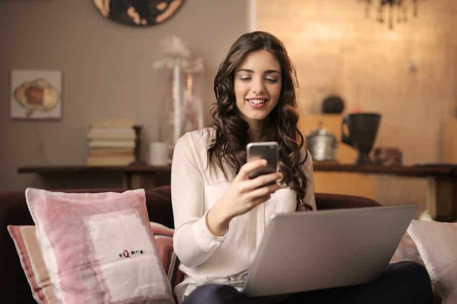 pexels-photo-920382-920382 A woman enjoying leisure time using her smartphone and laptop in a cozy living room.
